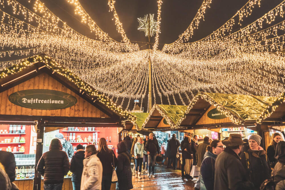 White Christmas light decorations with a star above the people and Christmas Market stalls 