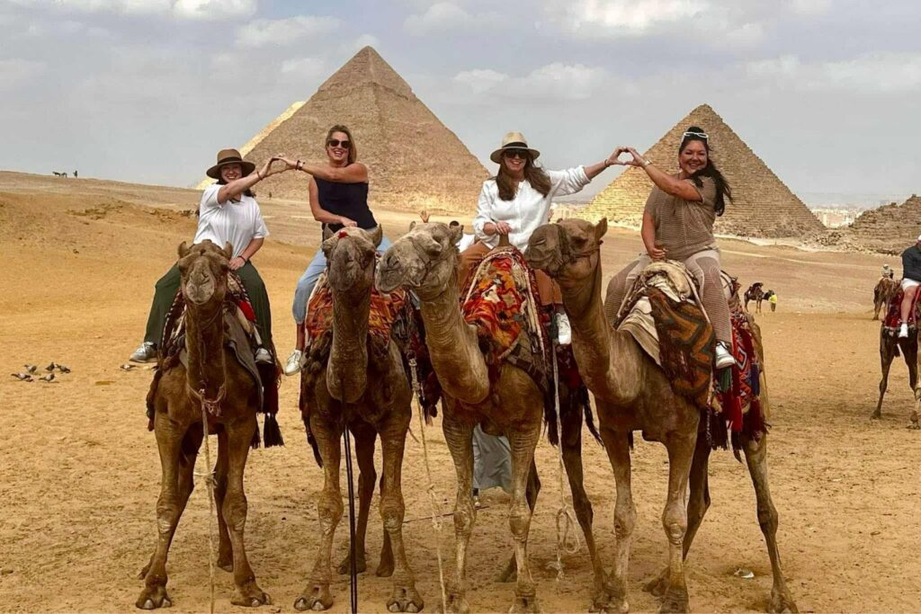 Travel Advisor Adventures by Terra riding on a camel with friends with pyramids of Giza in the background